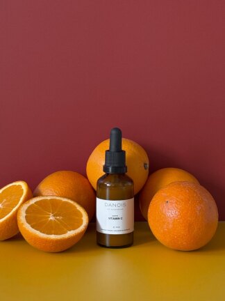 1 flaske vitamin C sammen med appelsiner på bord