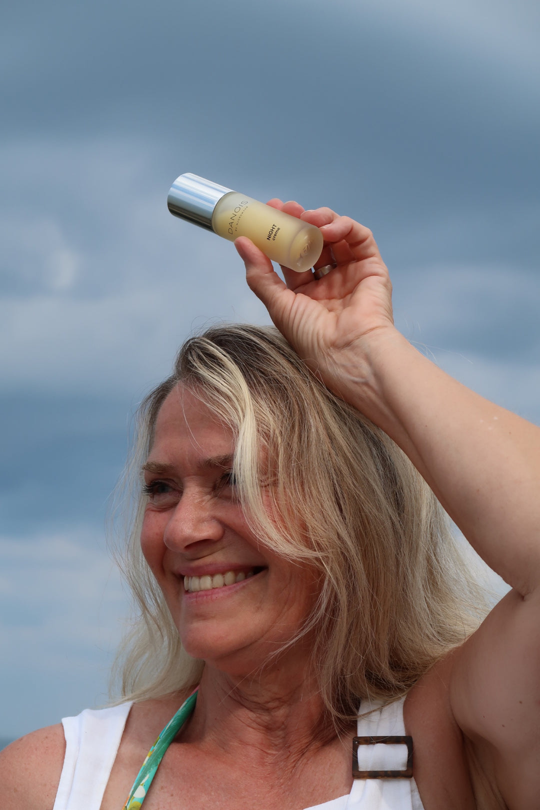 billedet viser en kvinde som holder DANOIS' Night Creme, hun har strandtøj på, baggrunden er en flot blå himmel. Det giver en sommer-vibe