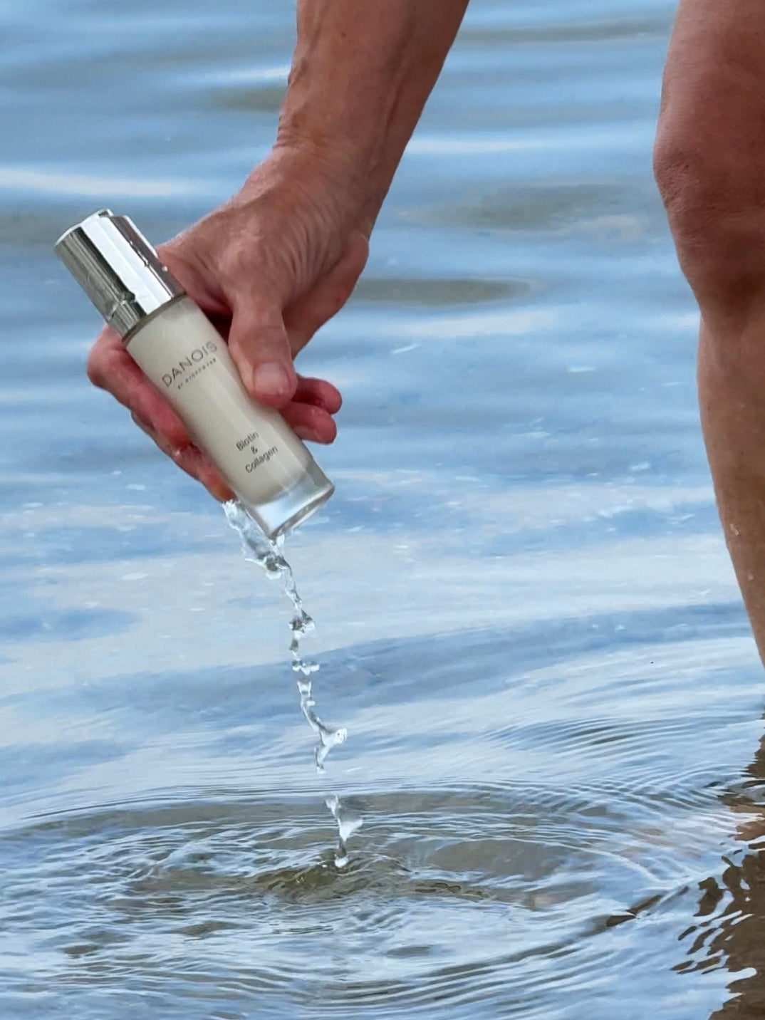 Billedet viser DANOIS' Biotin & Collagen som bliver taget op af vandet af en model nede på en strand.