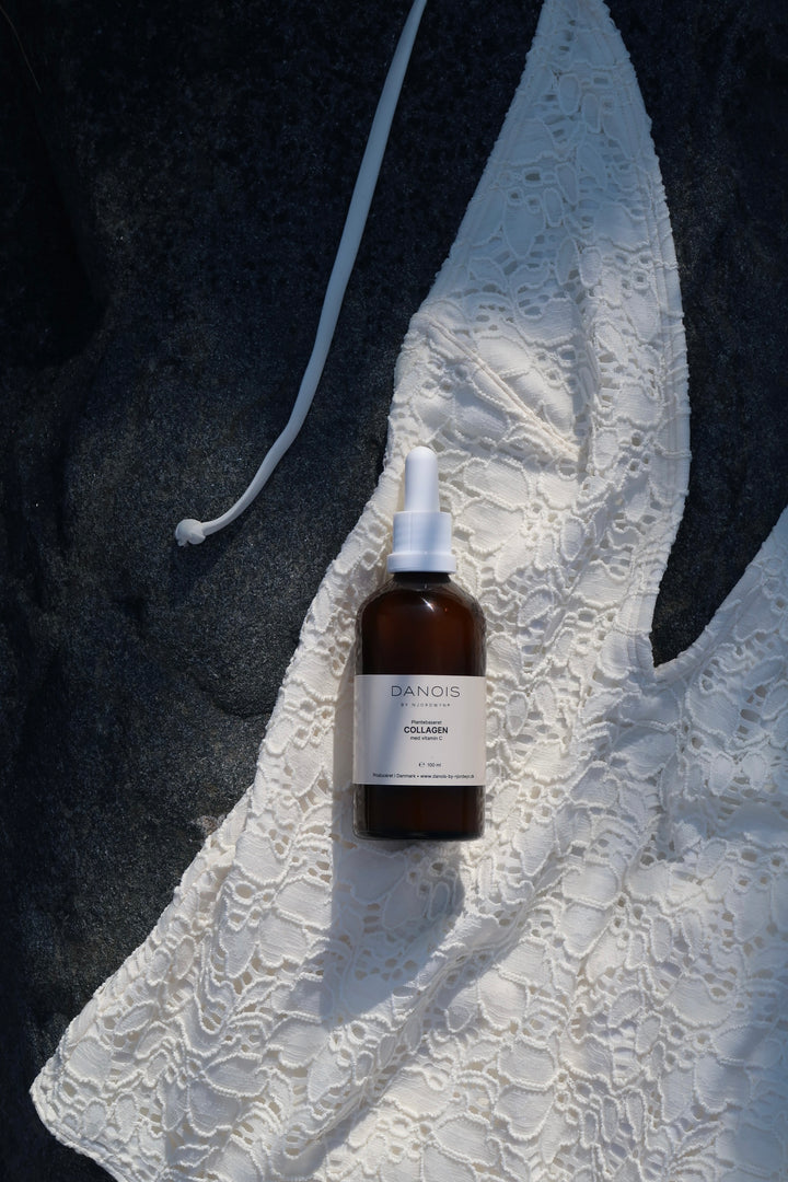 DANOIS' Plantebaseret Collagen ligger her på en hvid blonde badedragt i skyggen på en stor sten nede ved stranden.