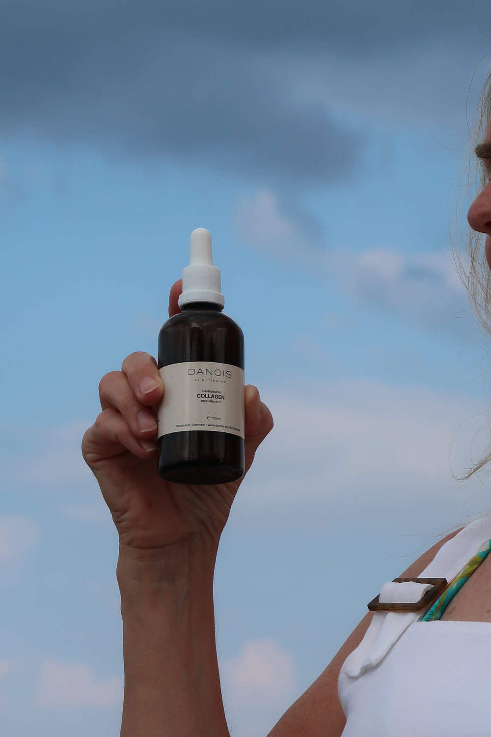 En model holder DANOIS' Plantebaseret Collagen, baggrunden er en smuk blå himmel